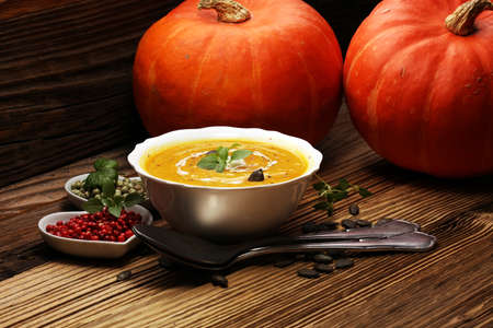 Roasted pumpkin and carrot soup with cream and pumpkin seeds on wooden backgroundの写真素材