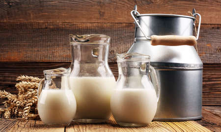 A jug of milk and glass of milk on a wooden table.の写真素材