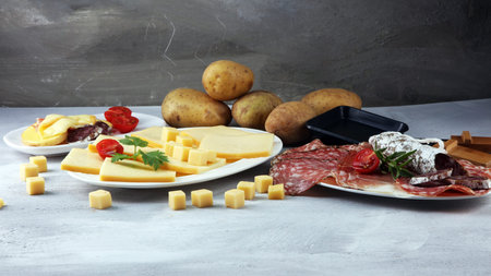 Delicious traditional Swiss melted raclette cheese on diced boiled or baked potato served in individual skillets with salami.の写真素材