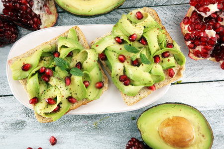 sliced avocado and ripe pomegranates on toast bread with spices and avocado