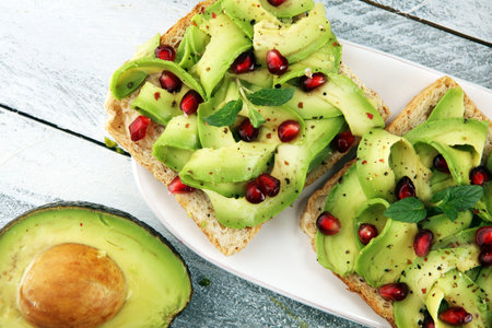 sliced avocado and ripe pomegranates on toast bread with spices and avocadoの写真素材