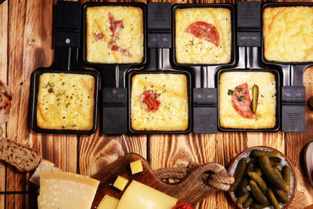 Delicious traditional Swiss melted raclette cheese served in individual skillets with salamiの写真素材