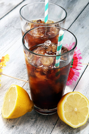 Softdrink with ice cubes, lemon and straw in glass.