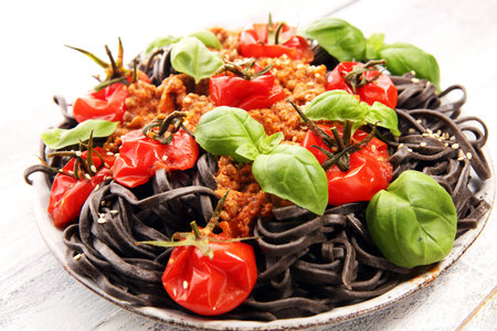 Fresh black tagliolini pasta. Fresh homemade pasta with basil and tomato on the rustic table.の写真素材