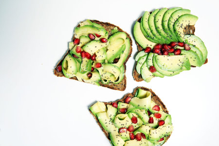 sliced avocado and ripe pomegranates on toast bread with spices and avocado 