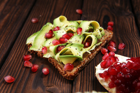 sliced avocado and ripe pomegranates on toast bread with spices and avocado