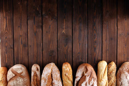 Assortment of baked bread and bread rolls on wooden table background. Bakery poster conceptの写真素材