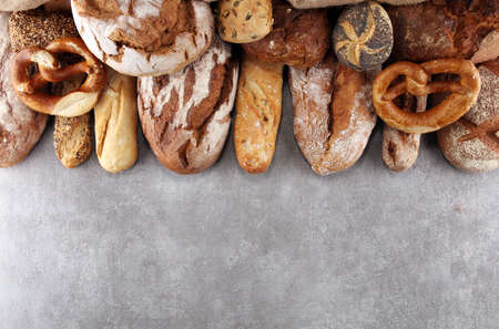 Assortment of baked bread and bread rolls on stone table background. Bakery poster conceptの写真素材