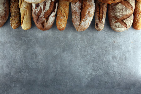 Assortment of baked bread and bread rolls on stone table background. Bakery poster concept
