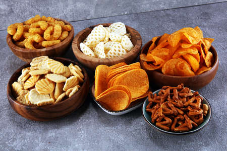 Salty snacks. Pretzels, chips, crackers in wooden bowls. Unhealthy products. food bad for figure, skin, heart and teeth. Assortment of fast carbohydrates food.の写真素材