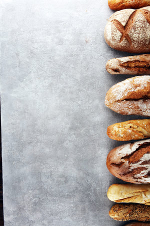 Assortment of baked bread and bread rolls on stone table background. Bakery poster concept