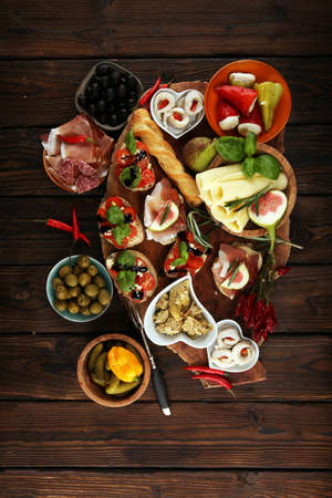 Italian antipasti wine snacks set. Cheese variety, Mediterranean olives, pickles, Prosciutto di Parma, tomatoes, artichokes on tableの写真素材