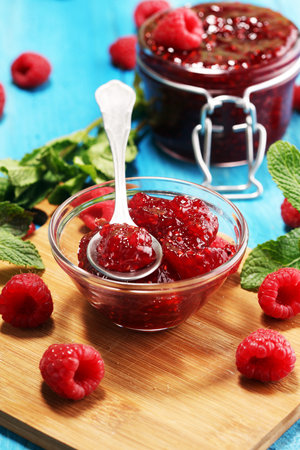 raspberry jam with fresh raspberries and mint. marmalade on spoon and jar on blue background