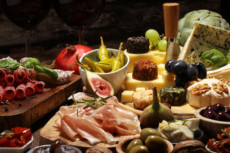 Italian antipasti wine snacks set. Cheese variety, Mediterranean olives, crudo, Prosciutto di Parma, salami and wine in glasses over wooden grunge backgroundの写真素材