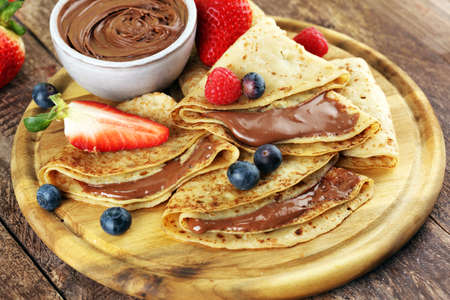 Delicious Tasty Homemade crepes with chocolate or pancakes with raspberries and blueberries on woodの写真素材