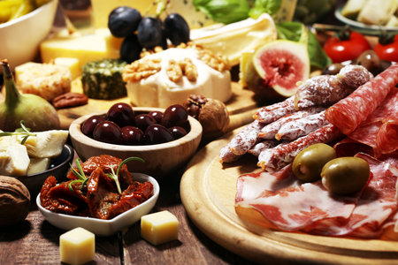 Italian antipasti wine snacks set. Cheese variety, Mediterranean olives, crudo, Prosciutto di Parma, salami and wine in glasses over wooden grunge backgroundの写真素材