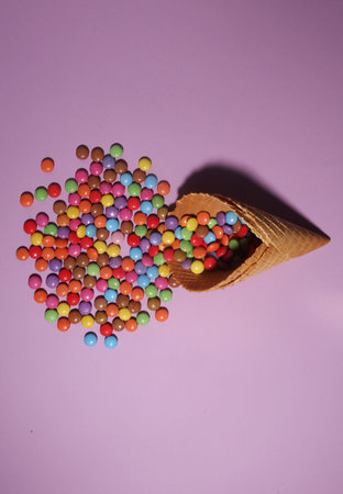 Ice cream waffle cone and scattering of multicolored sweets and confectionery topping on color...