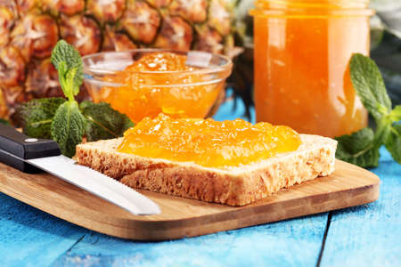 Toast bread with homemade pineapple jam or marmalade on rustic blue table served with butter for breakfast or brunchの写真素材