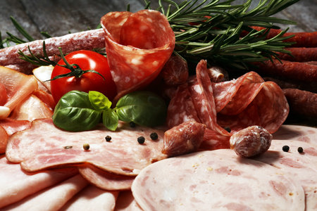 Food tray with delicious salami, pieces of sliced ham, sausage and salad. Meat platter with...