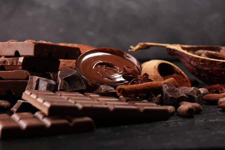 Melting chocolate or melted chocolate with a chocolate swirl and stack, chips and powder on dark...