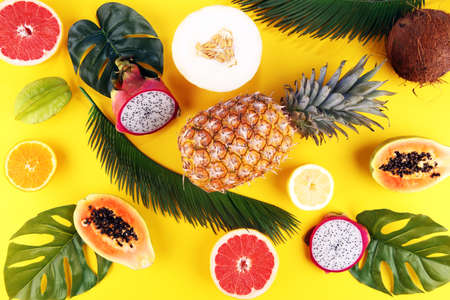 Exotic fruits and tropical palm leaves on pastel yellow background - papaya, mango, pineapple, banana, carambola, dragon fruit, lemon, orange, melon, coconut, lime.の写真素材