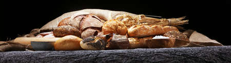 Assortment of baked bread and bread rolls on rustic table background.の写真素材