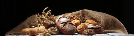 Assortment of baked bread and bread rolls on rustic table background.