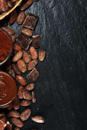 Melting chocolate or melted chocolate with a chocolate swirl and stack, chips and powder on dark tableの写真素材