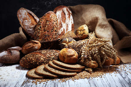 Assortment of baked bread and bread rolls on rustic table background.の写真素材