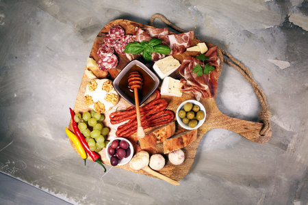 Cutting board with prosciutto, salami, coppa, cheese,bread sticks and olives on dark stone...