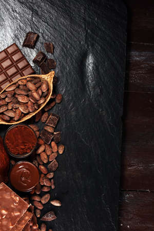 Melting chocolate or melted chocolate with a chocolate swirl and stack, chips and powder on dark tableの写真素材