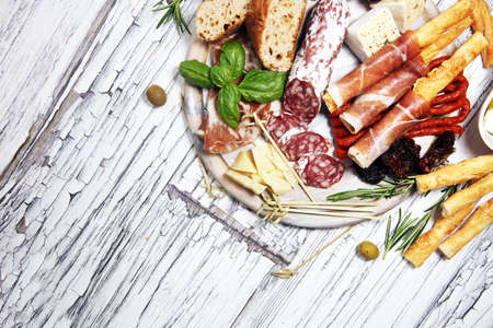 antipasto various appetizer. Cutting board with prosciutto, salami, coppa, cheese,bread sticks and olives on white woodenの写真素材