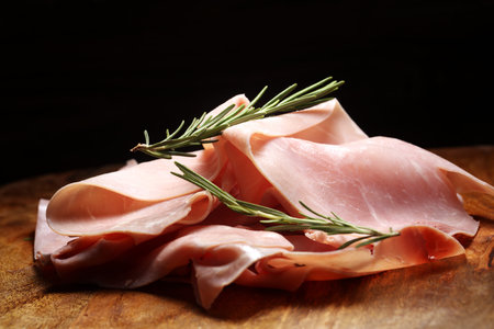 Sliced ham on wooden background. Fresh prosciutto. Pork ham sliced with rosemary. cutting cold meat