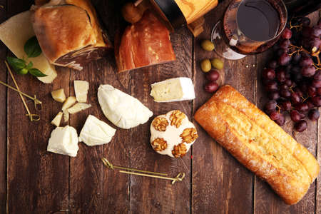 Antipasto and red wine. Still life in a rustic style. Grapes on a wooden table with a bottle of wine and exquisite meat and cheese.の写真素材