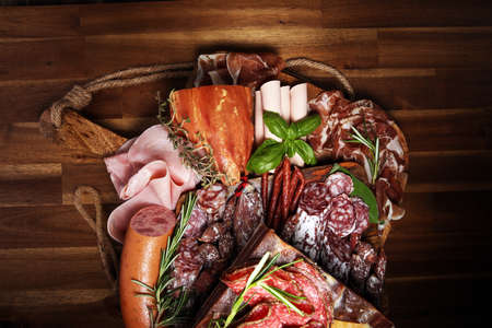 cold meat assortment with delicious salami and herbs . Variety of meat products including coppa and sausages on woodの写真素材