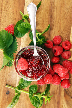 raspberry jam with fresh raspberries and mint. marmalade on spoon and jar on wooden background