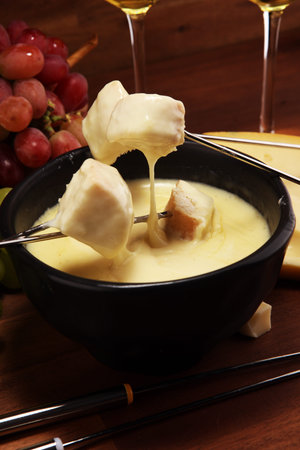 Gourmet Swiss fondue dinner on a winter evening with assorted cheeses on a board alongside a heated pot of cheese fondue with forks dipping breadの写真素材