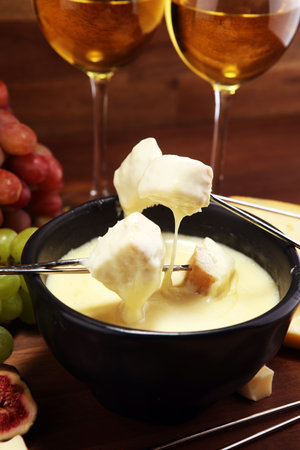 Gourmet Swiss fondue dinner on a winter evening with assorted cheeses on a board alongside a heated...
