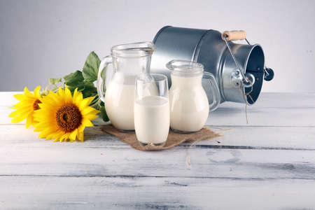 A jug of milk and glass of milk on a wooden table and sunflowerの写真素材
