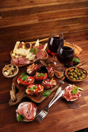 Italian antipasti wine snacks set. Cheese variety, Mediterranean olives, pickles, Prosciutto di Parma, tomatoes, artichokes on tableの写真素材