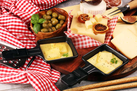 Delicious traditional Swiss melted raclette cheese on diced boiled or baked potato served in individual skillets with salami.の写真素材