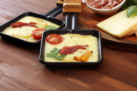 Delicious traditional Swiss melted raclette cheese on diced boiled or baked potato served in individual skillets with salami.の写真素材