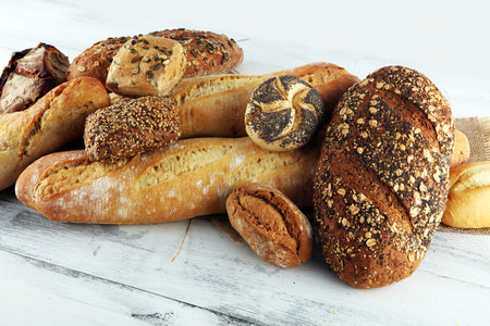 Assortment of baked bread and bread rolls on wooden table background. Bakery poster concept