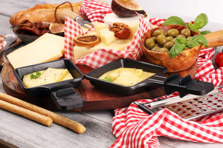 Delicious traditional Swiss melted raclette cheese on diced boiled or baked potato served in individual skillets with salami.の写真素材