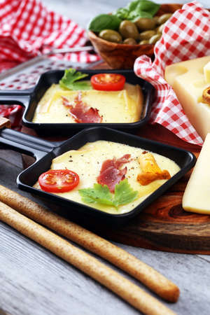 Delicious traditional Swiss melted raclette cheese on diced boiled or baked potato served in individual skillets with salami.の写真素材
