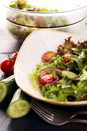 bowl of salad with vegetables and greens, with tomato, cucumber and onions on tableの写真素材