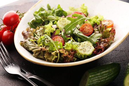 bowl of salad with vegetables and greens, with tomato, cucumber and onions on table
