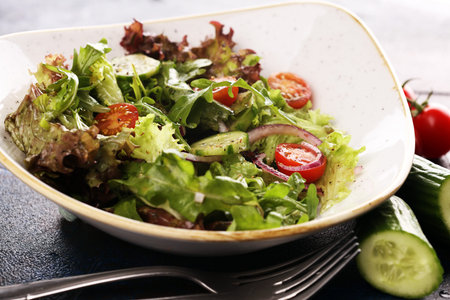 bowl of salad with vegetables and greens, with tomato, cucumber and onions on table