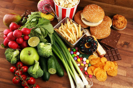 healthy or unhealthy food. Concept photo of healthy and unhealthy food. Fruits and vegetables vs donuts,sweets and burgers on darkの写真素材