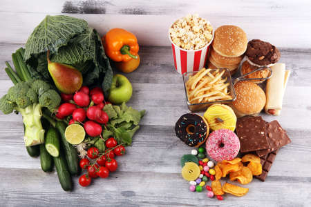 healthy or unhealthy food. Concept photo of healthy and unhealthy food. Fruits and vegetables vs donuts,sweets and burgers on darkの写真素材